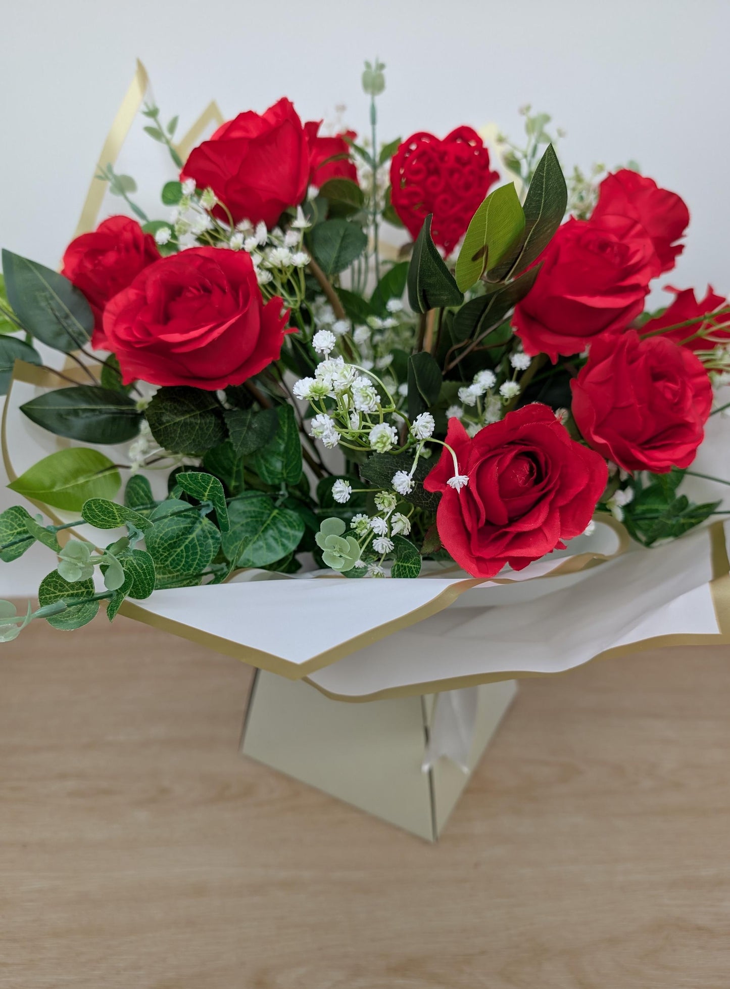 Bouquet of red roses with green leaves on a white stand against a light background