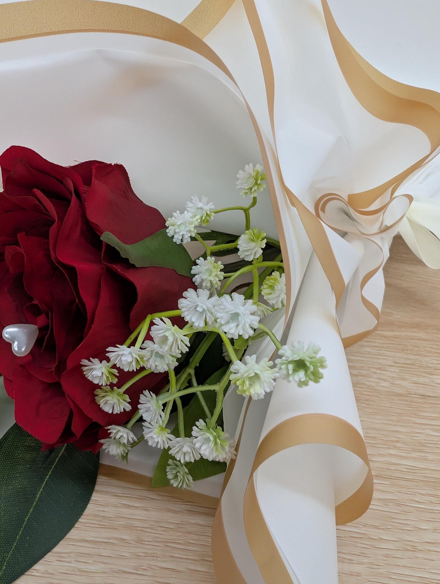Bouquet of red roses and white flowers with gold ribbon on a wooden surface