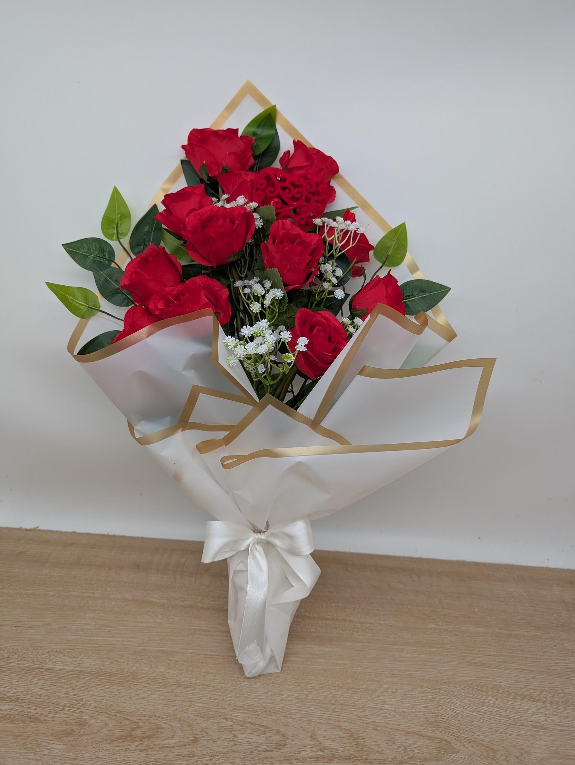 Bouquet of red roses with greenery in a decorative box on a wooden surface.