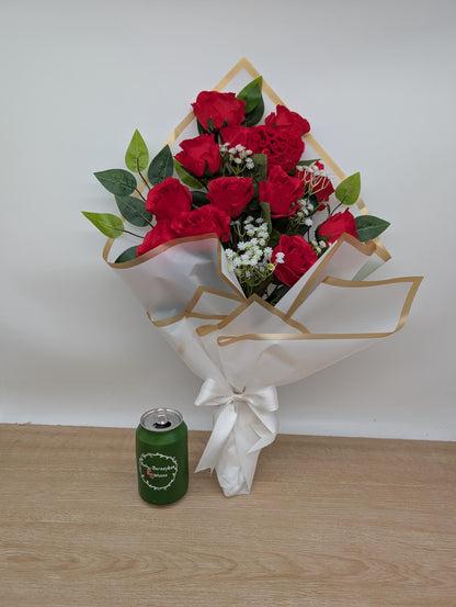 Bouquet of red roses with greenery and a green can on a wooden surface.