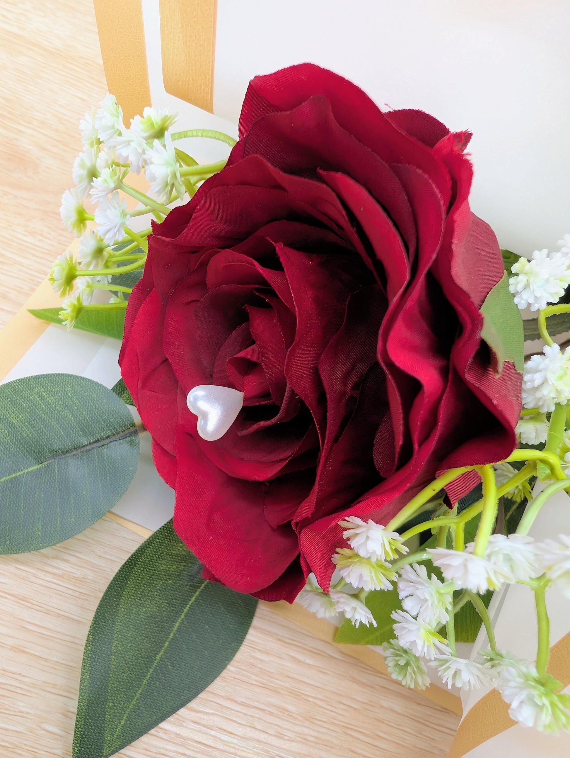 Red rose with green leaves and white flowers on a wooden surface