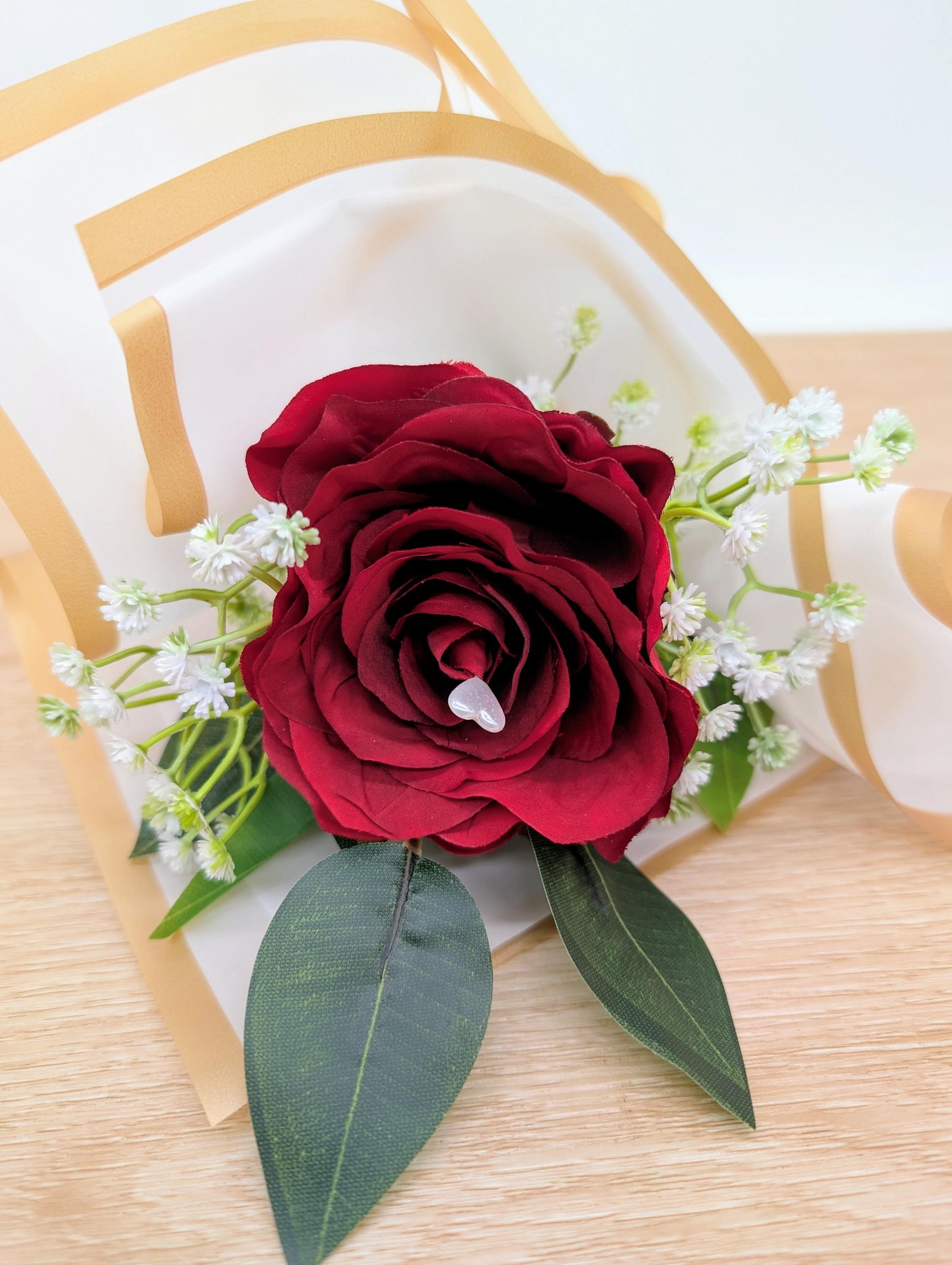 Red rose with green leaves and white flowers on a wooden surface