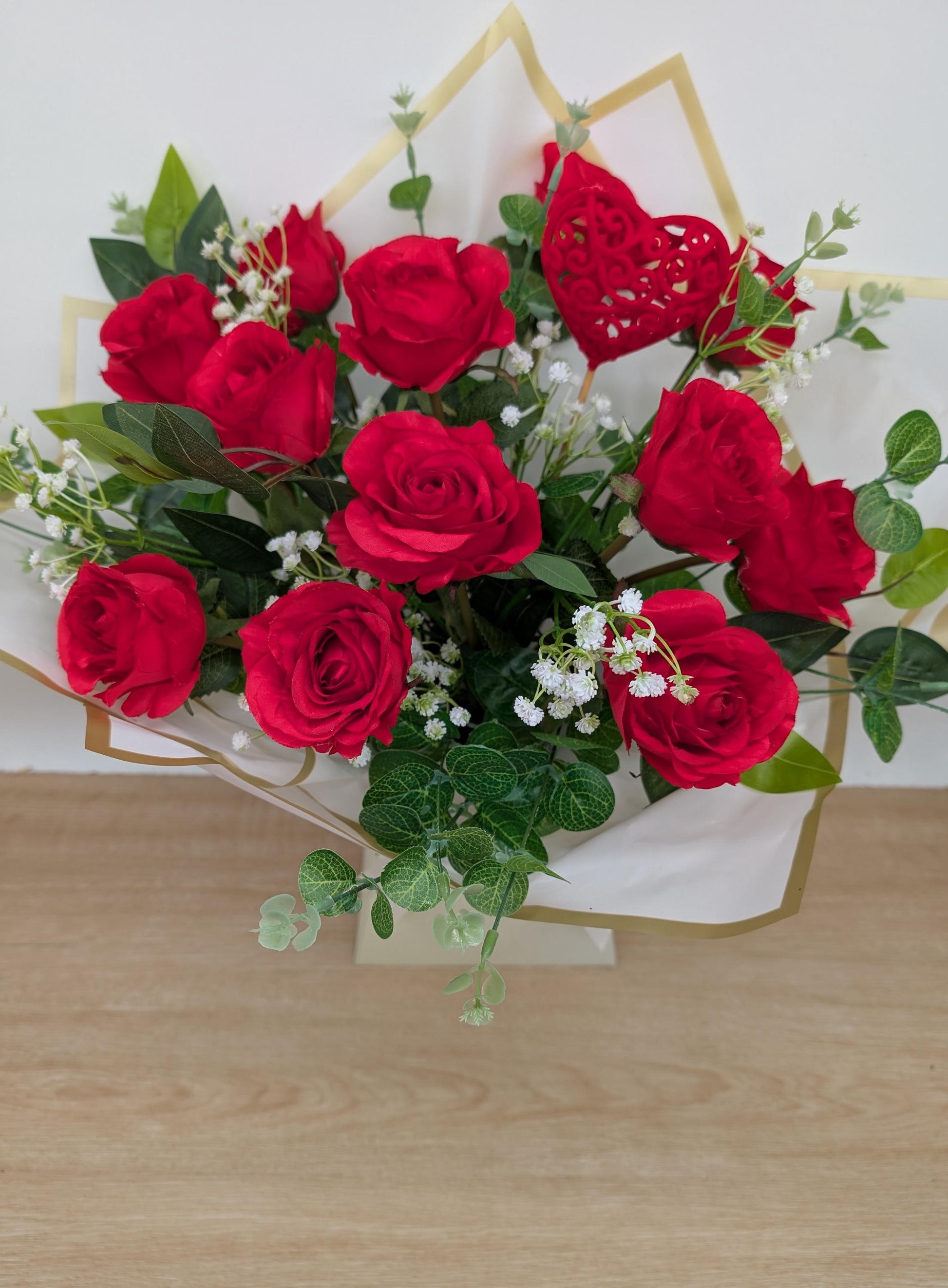 Bouquet of red roses with green leaves on a wooden surface