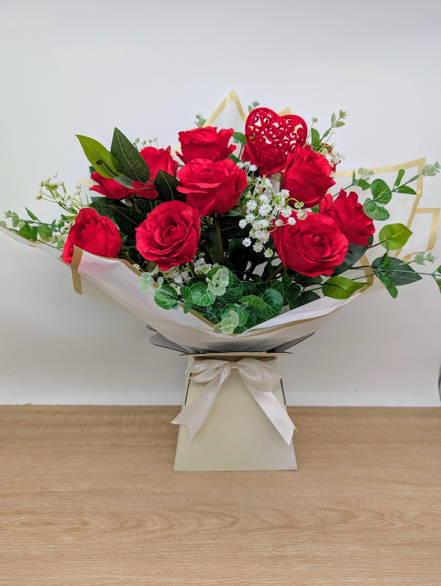 Bouquet of red roses with greenery on a wooden surface