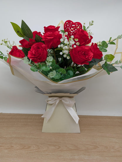Bouquet of red roses wrapped in white paper with a bow on a wooden surface.
