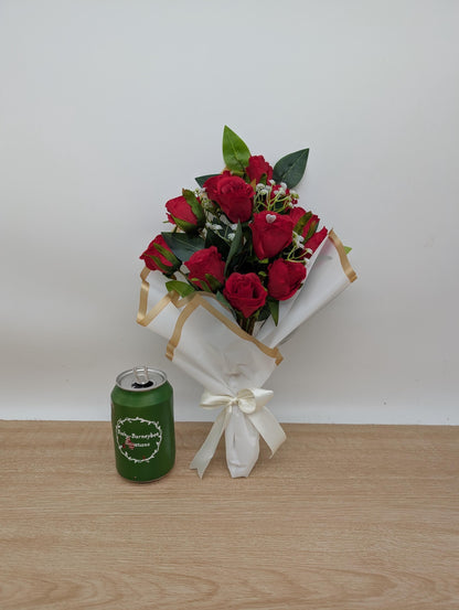 Bouquet of red roses and a green canister with a white ribbon on a wooden surface.