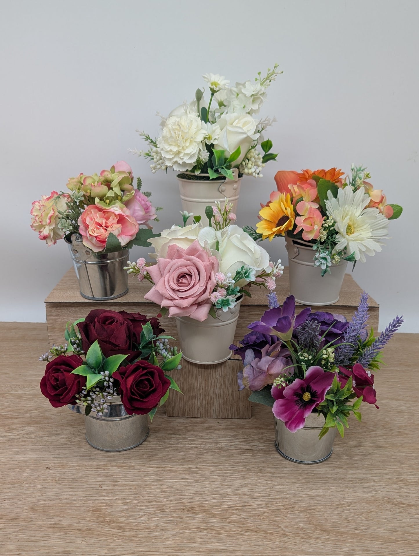 Set of artificial flower arrangements in small pots on a wooden surface.