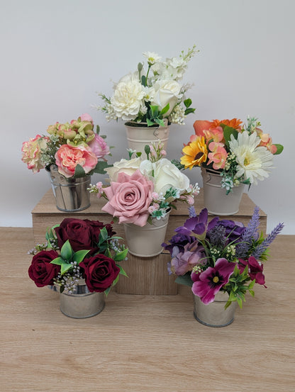 Set of artificial flower arrangements in small pots on a wooden surface.