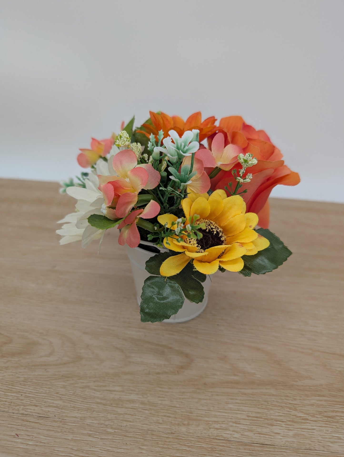 Artificial flower arrangement in a white vase on a wooden surface with a light background