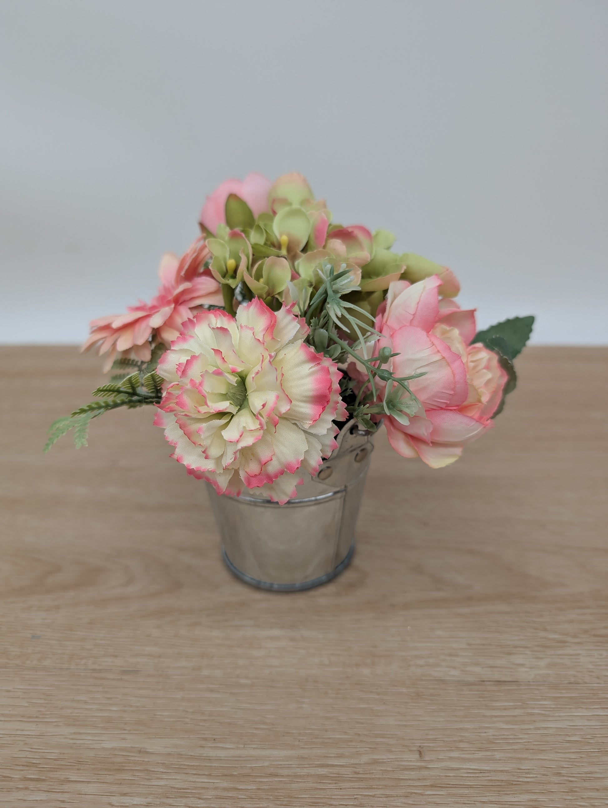 Small potted plant with pink and green flowers on a wooden surface