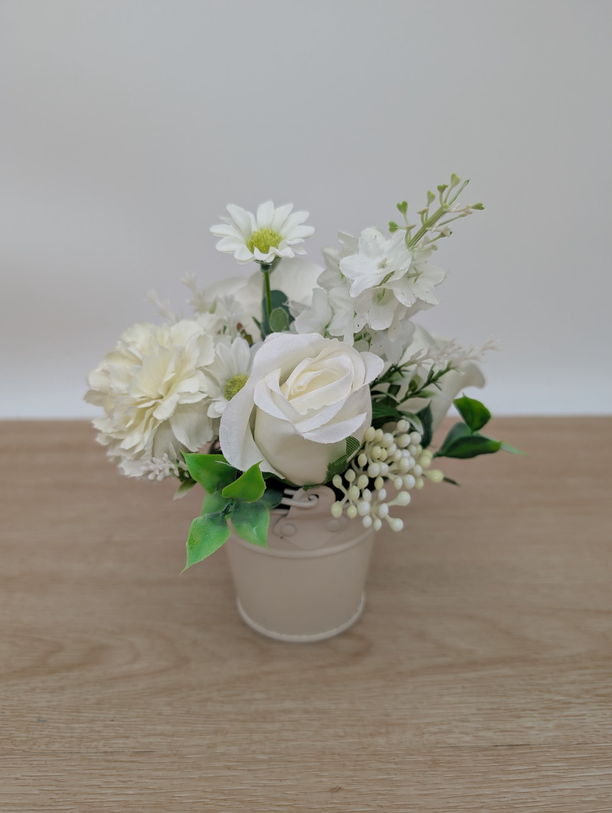 Small potted plant with white flowers on a wooden surface