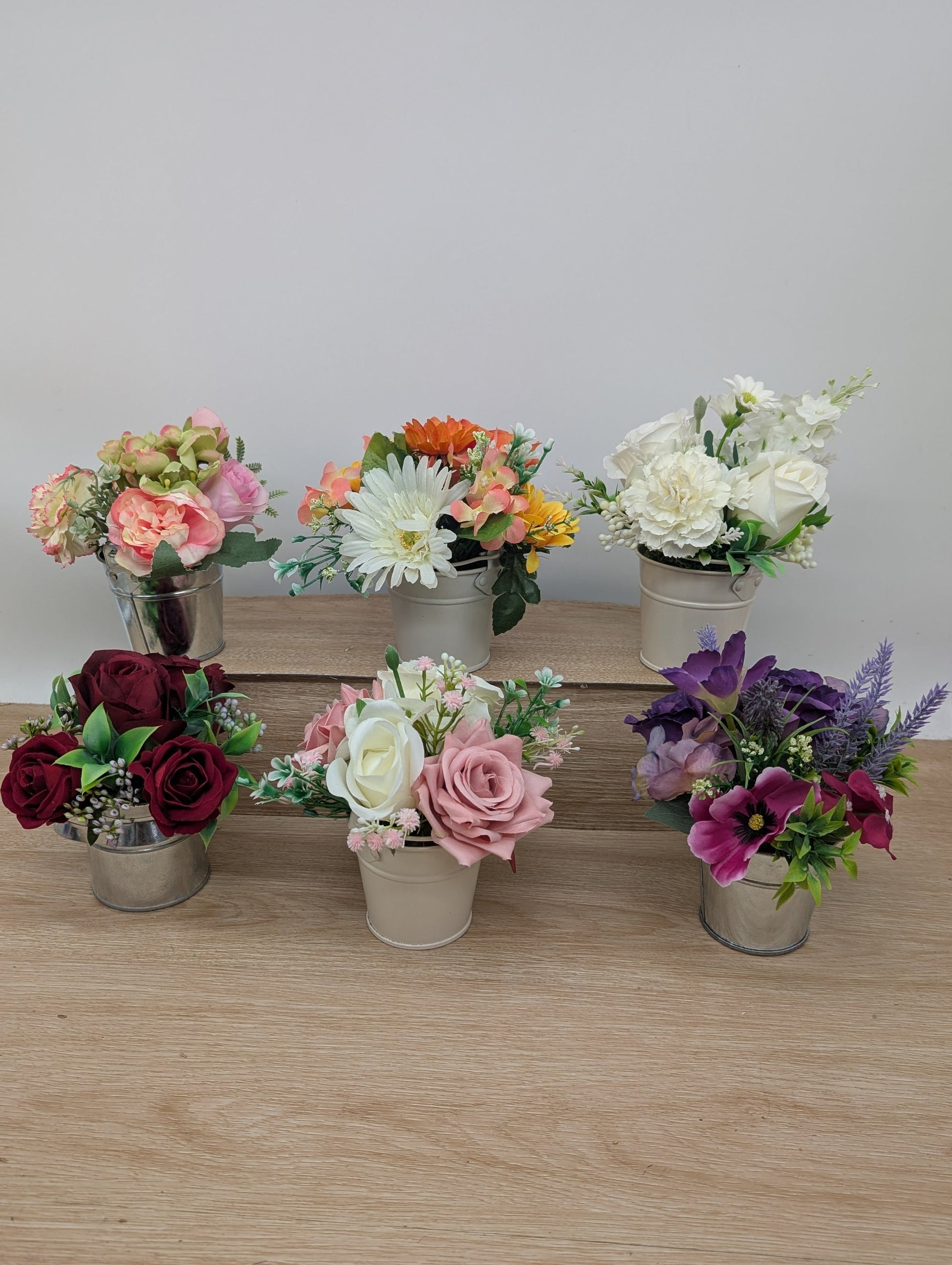 Set of six small potted floral arrangements on a wooden surface with a white background