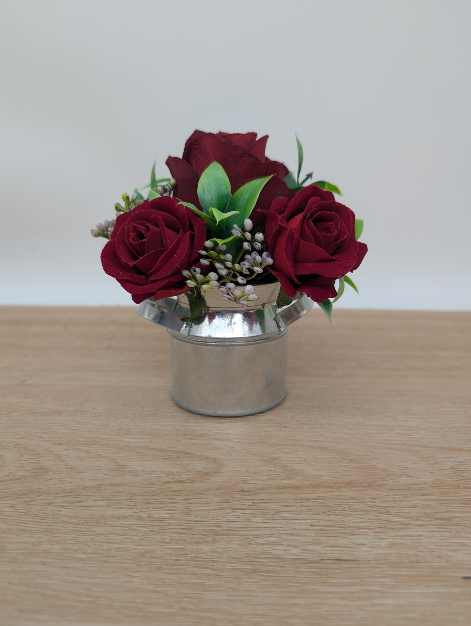 Small silver bucket with red roses on a wooden surface