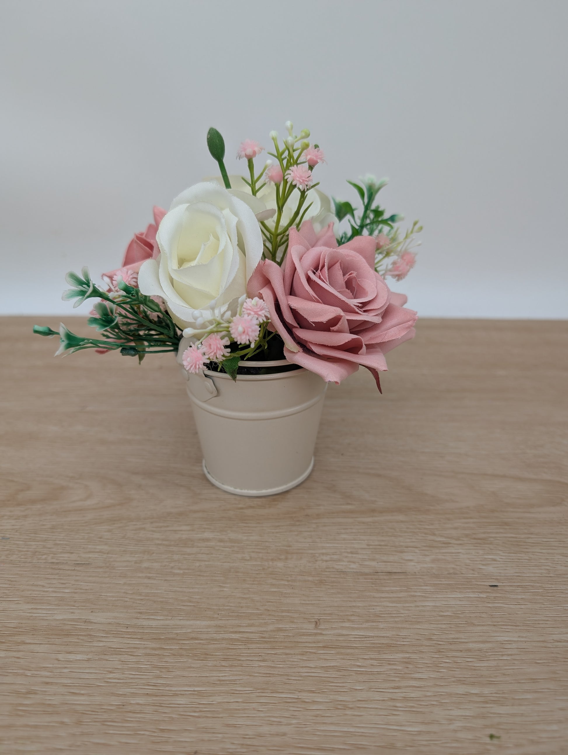 Small potted plant with pink and white flowers on a wooden surface